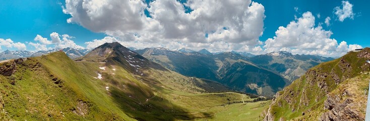 Panoramic view of Alpine mountains with green hills and blue sky in summer
