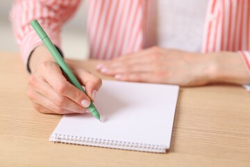 Naklejka premium Woman writing in notepad with pen at wooden table, closeup