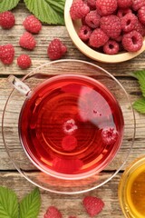 Tasty raspberry tea, berries and leaves on wooden table, flat lay