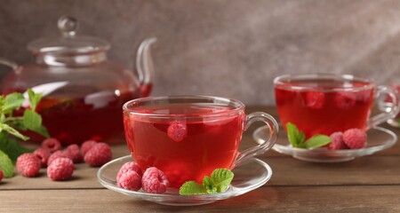 Tasty raspberry tea in glass cups, teapot, berries and mint on wooden table, closeup