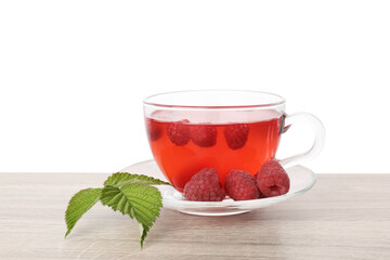 Tasty raspberry tea in glass cup, berries and green leaves on wooden table against white background