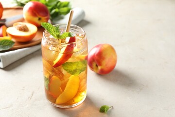 Refreshing iced peach tea with mint in glass and fresh fruits on white table, closeup. Space for text