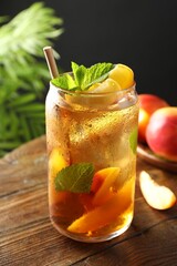 Refreshing iced peach tea with mint in glass and fresh fruits on wooden table, closeup