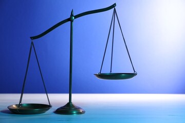 Scales of justice on table against blue background