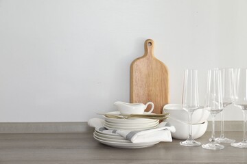 Different clean white dishware, cutting board, glasses and cutlery on counter in kitchen. Space for text