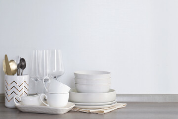 Different clean white dishware, glasses and cutlery on counter in kitchen