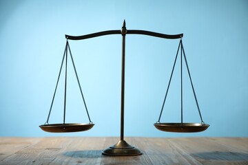 Scales of justice on wooden table against light blue background