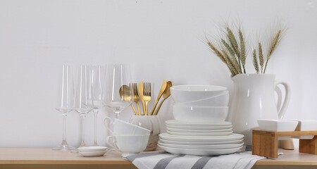 Different clean white dishware, glasses, cutlery and spikes on wooden table indoors