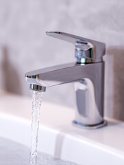 Modern chrome faucet pouring water into sink in bathroom