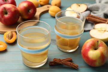 Tasty compot in glasses, fresh apples, apricots and cinnamon on light blue wooden table, closeup