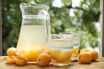 Tasty compot with apples in glasses, jug and fresh apricots on wooden table outdoors