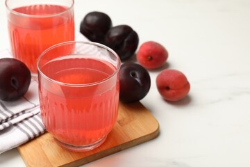 Tasty compot in glasses, plums and apricots on white marble table, closeup. Space for text