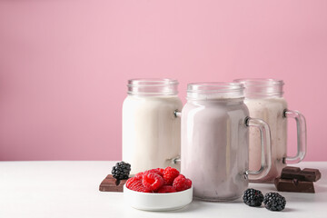 Different tasty milkshakes in mason jars and ingredients on white table, space for text