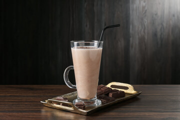 Tasty milkshake in glass and pieces of chocolate on wooden table