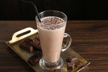 Tasty milkshake in glass and pieces of chocolate on wooden table, closeup