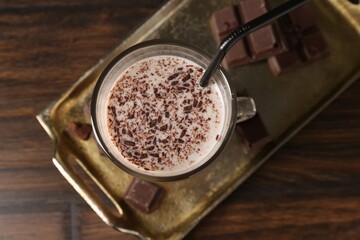 Tasty milkshake in glass and pieces of chocolate on wooden table, top view
