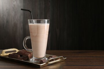 Tasty milkshake in glass and pieces of chocolate on wooden table, space for text