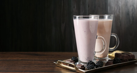 Different tasty milkshakes in glasses and ingredients on wooden table, space for text