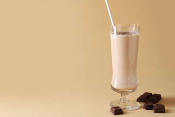 Tasty milkshake in glass and pieces of chocolate on beige background, space for text