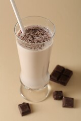 Tasty milkshake in glass and pieces of chocolate on beige background, closeup
