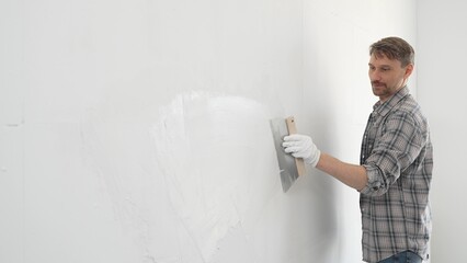 Male construction worker wearing protective gloves and plaid shirt, spreading plaster smoothly...