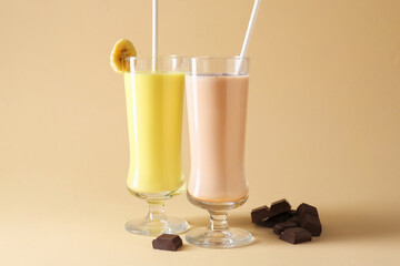 Different tasty milkshakes in glasses and pieces of chocolate on beige background