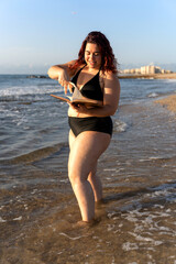 Curvy woman reading a book on the beach at sunset