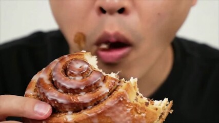 A close-up of a person messily eating a delicious gooey cinnamon roll with icing - Powered by Adobe