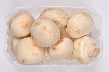 Fresh white mushrooms, or champignons, are packaged in a clear plastic container, shown against a white background