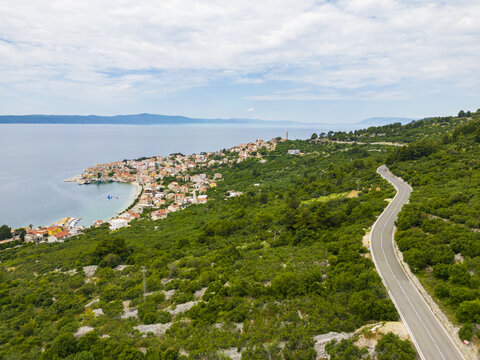 Aerial view of the winding road leading to the coastal town nestled between the lush green hills and the azure sea, Igrane, Split-Dalmatia County, Croatia.