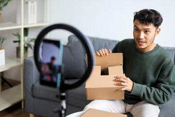 Young Male Influencer Explaining Product During Live Unboxing Video And Holding Cardboard Box