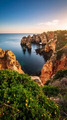 Coastal landscape at sunrise. Rocky shoreline meets the calm sea. Lush vegetation at the edge of the cliffs