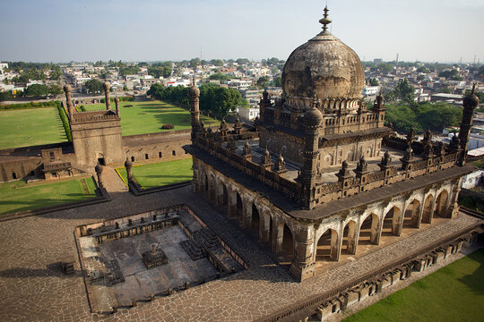 Aerial view of Ibrahim Rauza's intricate stonework bathed in the warm glow of the sun, contrasting against the lush green lawns and distant city, Bijapur, Karnataka, India.