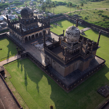 Aerial view of the Ibrahim Rouza complex with its weathered domes and lush green lawns casting long shadows under the sun, Bijapur, Karnataka, India.