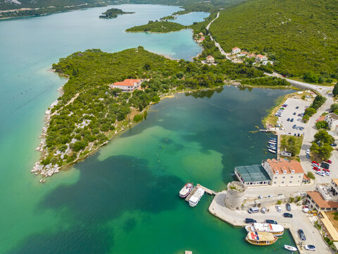 Aerial view of turquoise waters meeting ancient stone walls and red-tiled roofs under the Croatian sun, Mali Ston, Dubrovnik-Neretva County, Croatia.