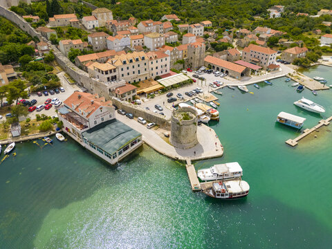 Aerial view of the ancient stone walls embracing the town and the glimmering turquoise harbor dotted with boats, Mali Ston, Dubrovnik-Neretva County, Croatia.