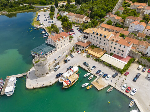 Aerial view of the ancient stone tower guarding the harbor, where boats rest on the turquoise water, contrasting with the terracotta roofs of Mali Ston, Dubrovnik-Neretva County, Croatia.