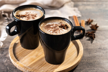 Chai Latte in Black Mug with Spices( star anise and cinnamon) on wooden table