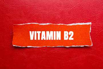Vitamin B2 message written on ripped torn orange paper piece on red background. Conceptual Vitamin...