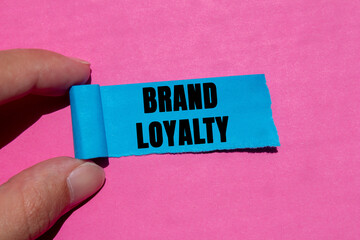 Brand loyalty message written on ripped torn blue paper piece on pink background. Conceptual brand...