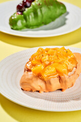 Two croissants, one with mango and the other with pistachio and cherries, are served on white plates against a yellow background.