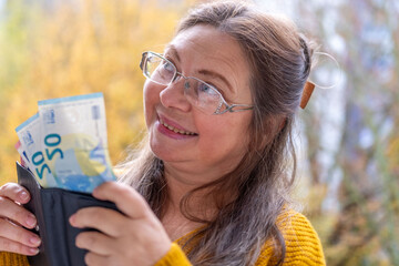 Mature white woman 50 years old, presenting, counts euro banknotes in hand, cash payments, savings,...