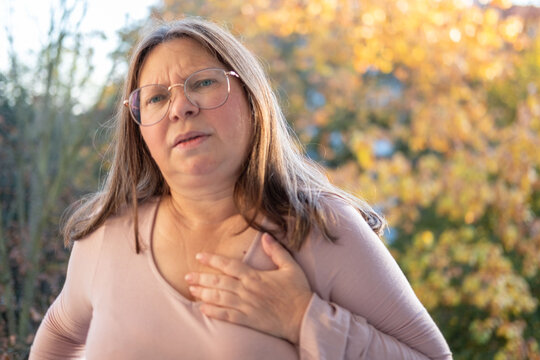 Middle-aged woman experiencing chest pain, pressing hands to heart. Concept of health problems, cardiac arrest, and distress, Health risk, heart failure, and emergency situation