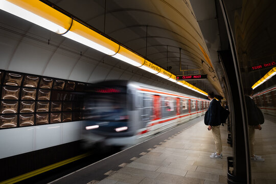 A Prague metro train arrives at Narodni trida station, with passengers waiting on the tiled platform as its motion blurs past