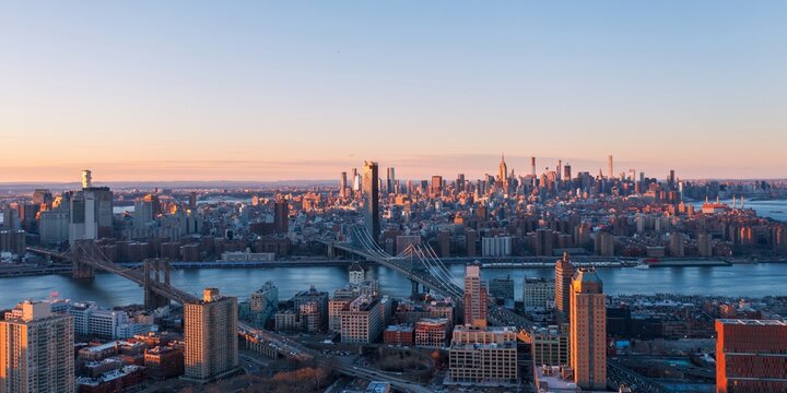 Aerial view of bridges span the river towards a distant skyline with the Empire State Building catching the warm glow of the setting sun,  New York, United States.