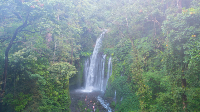 Aerial view of the cascading Tiu Kelep Waterfall plunges amidst a verdant embrace of dense foliage and mist-laden air, creating a serene oasis, Senaru, West Nusa Tenggara, Indonesia.