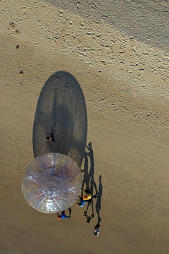 Mangaluru, India - 17 January 2010: Aerial view of a transparent zorb ball casting a dramatic shadow on the sandy beach, figures moving around it.