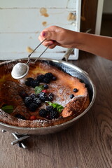 Traditional Dutch baby pancake served for breakfast, a popular European dish. The fluffy baked pancake is topped with fresh fruit, powdered sugar, and mint leaves, beautifully styled on a light.