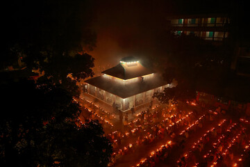 Narayanganj, Bangladesh - 16 November 2021: Aerial view of a luminous gathering around a building, its warm lights contrasting against the dark, hazy night sky.