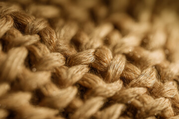 Close-up of beige knitted fabric showing detailed texture and soft yarn strands, highlighting cozy and warm textile material in natural light.